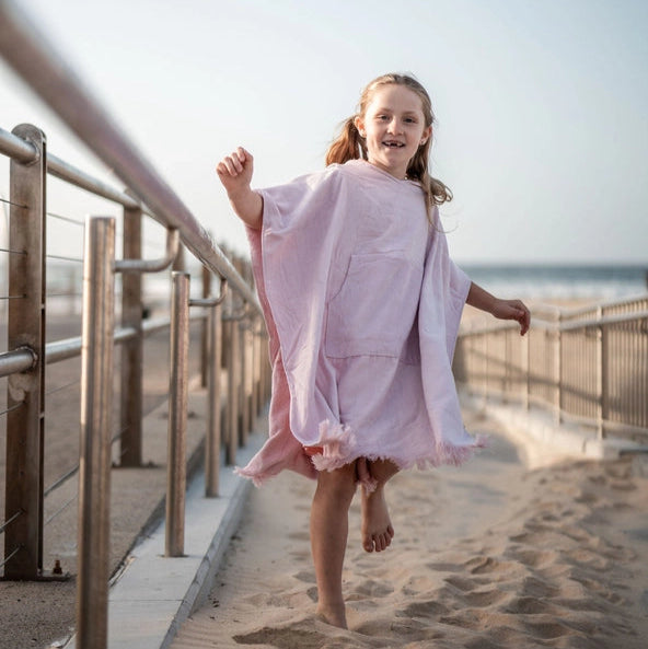 Young girl in a pink kids Hooded towel running on a wooden boardwalk near the beach.