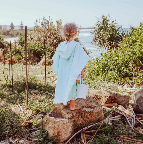 Young girl in a pink kids Hooded towel running on a wooden boardwalk near the beach.