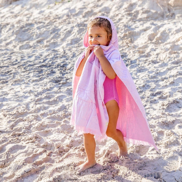Young girl in a pink kids Hooded towel running on a wooden boardwalk near the beach.