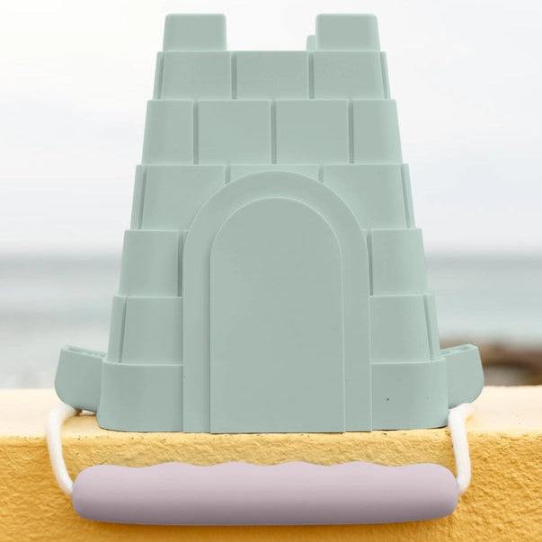 Green sandcastle mold on a yellow surface with a blurred beach background