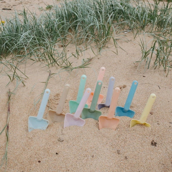 Colorful plastic shovels on a sandy beach with grasses in the background