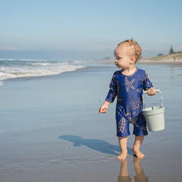 Child in a blue dress holding a bucket on a beach
