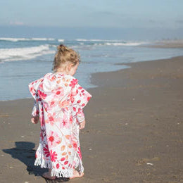 Child in a floral towel standing on a beach with waves in the background