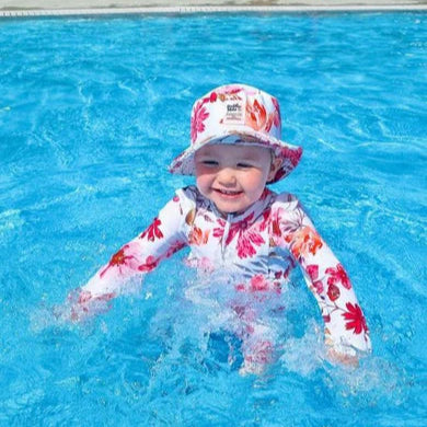 Child in a floral swimsuit and hat playing in a pool