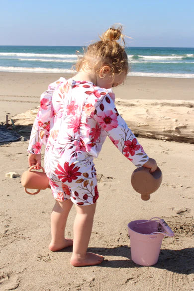 Child in a floral swimsuit playing on a beach with sand toys.