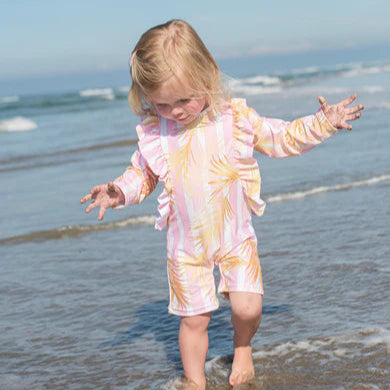 Child in a colorful swimsuit playing in the ocean with a clear blue sky.