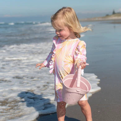Child in a colorful dress standing on a beach with ocean waves in the background