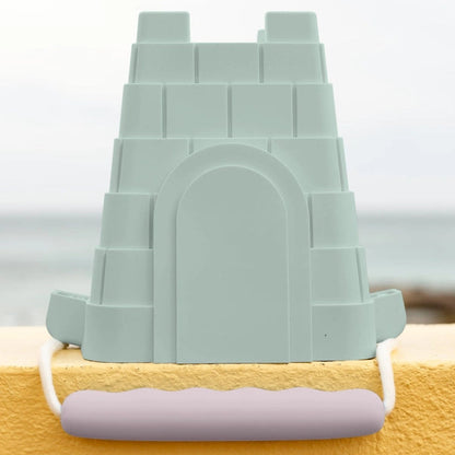 Green sandcastle mold on a yellow surface with a blurred beach background