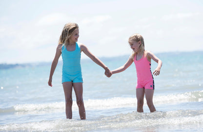 Two young girls holding hands in the ocean with a clear sky.
