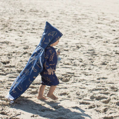 Child wearing a blue hooded towel with star patterns on a sandy beach.
